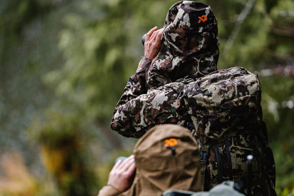 Close-up shot of a First Lite merino wool base layer showing the texture, with a hunter in the background.